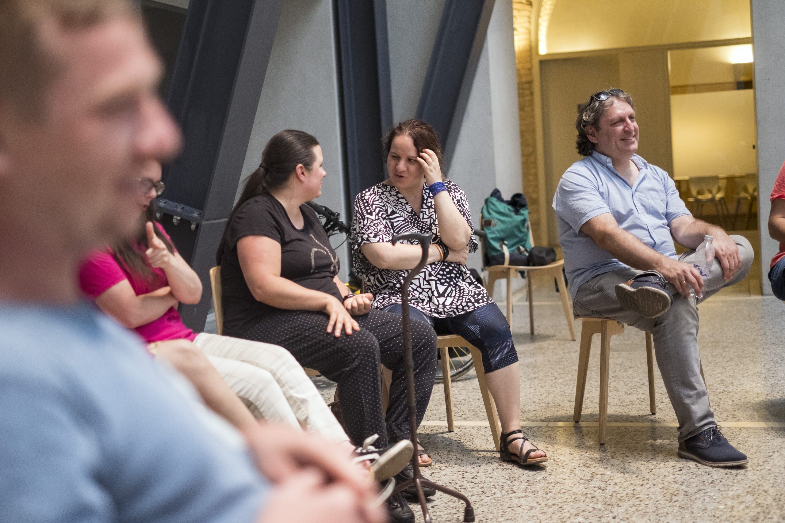 Résztvevők egy csoportja székeken ülve, mosolyogva és kötetlenül beszélgetve egy beltéri rendezvényen.